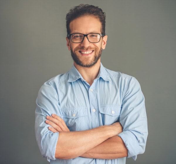 Man in glasses and button down shirt smiling at the camera with arms crossed