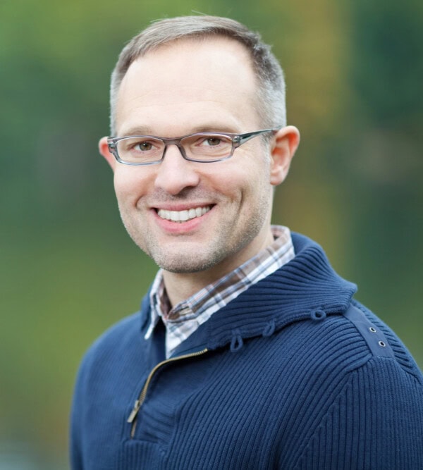 Man with glasses and a sweater smiling at the camera